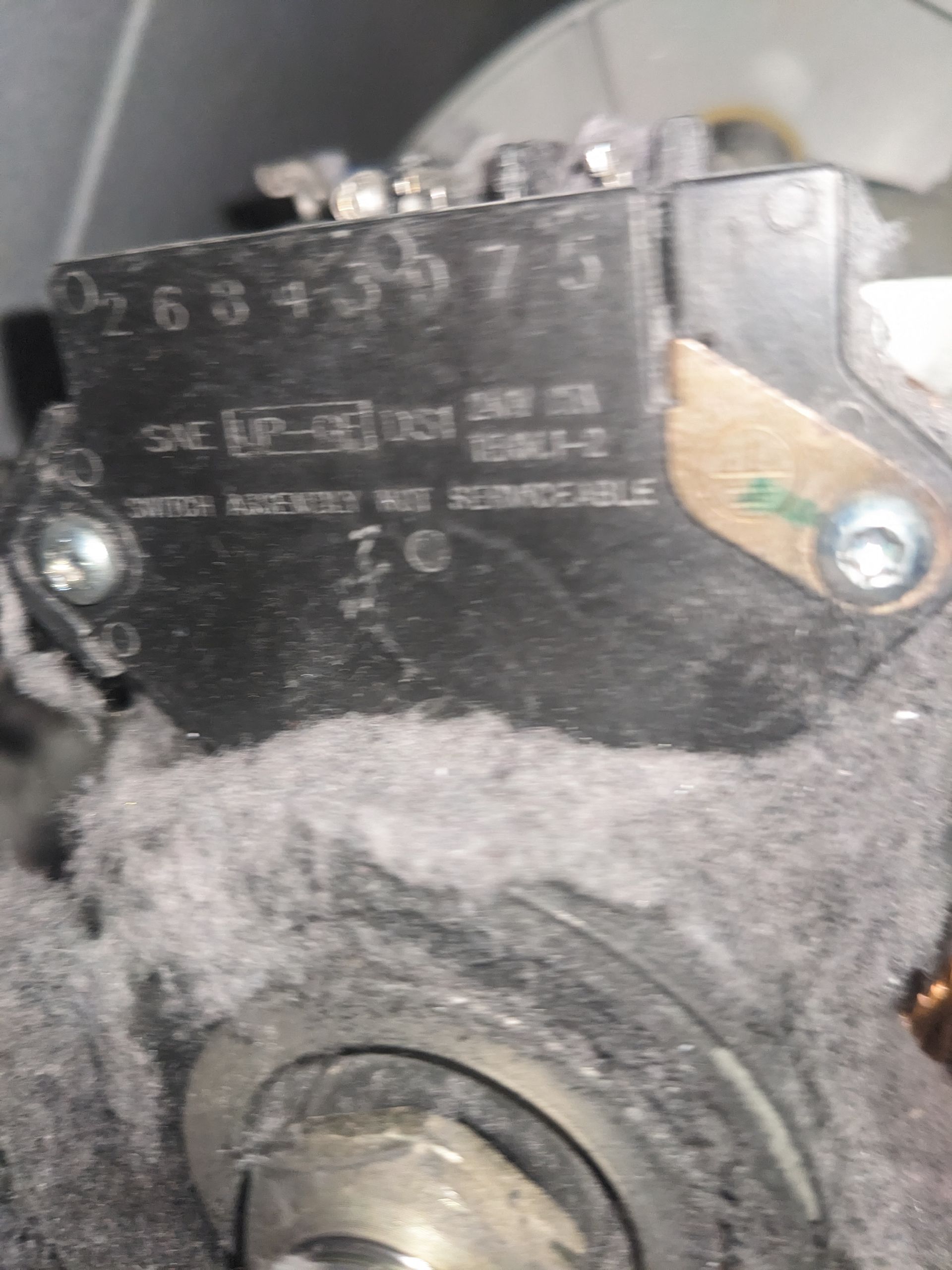 Close-up of a black metal mechanical part with a worn label and a central bolt, coated in dust and grime
