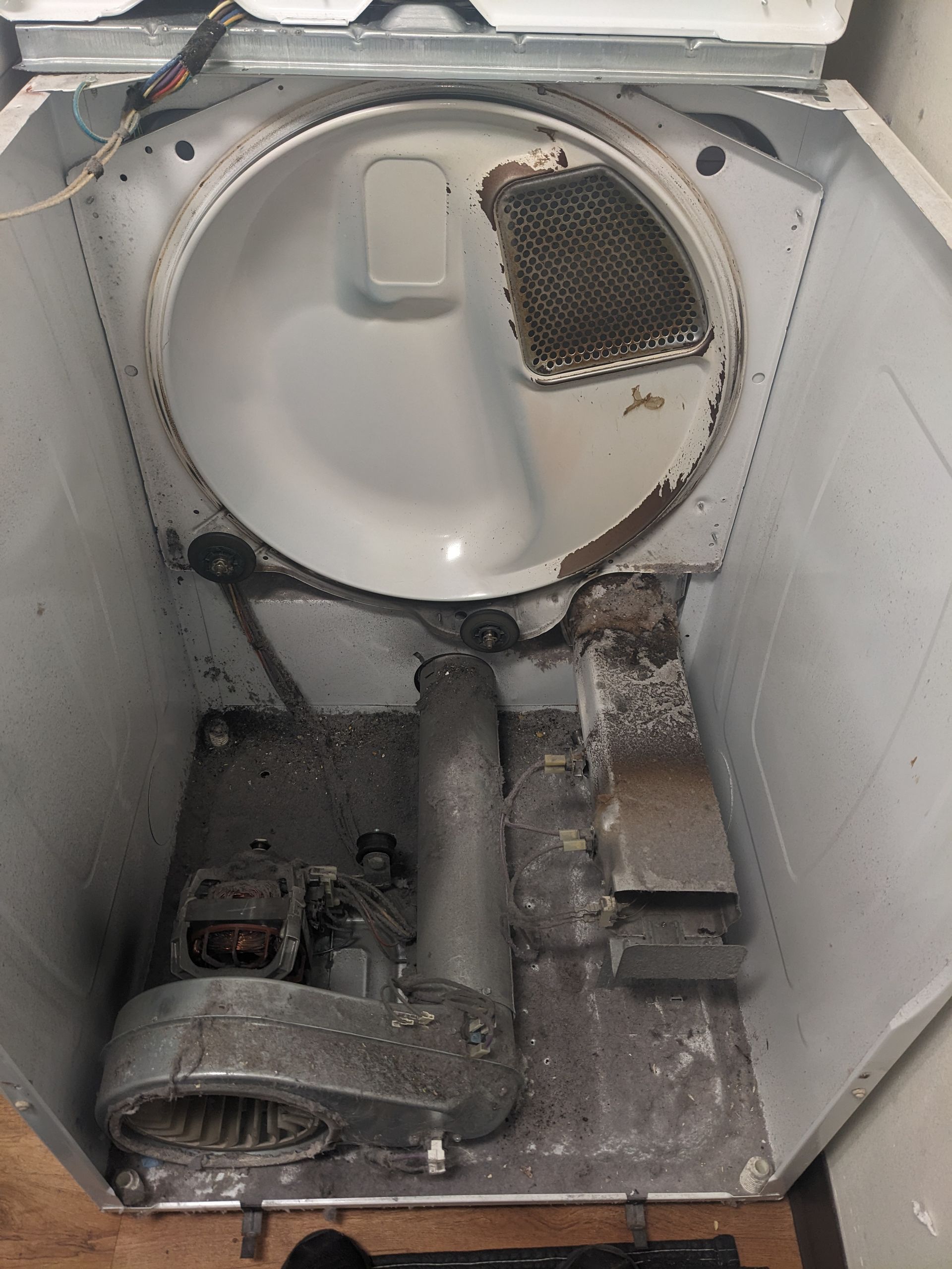 Inside a dryer, a detached drum with lint and debris scattered in the metal interior.