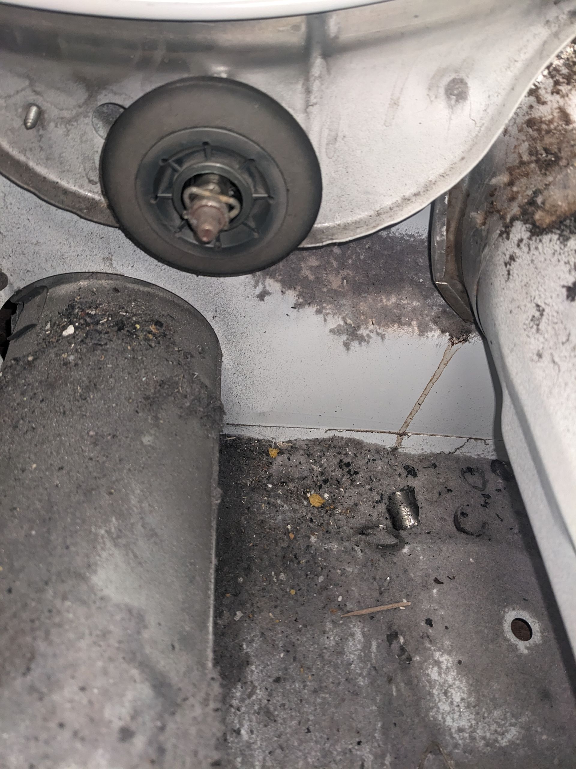 Dirty industrial machine compartment with a large bolt, grease, and debris on a metal floor.