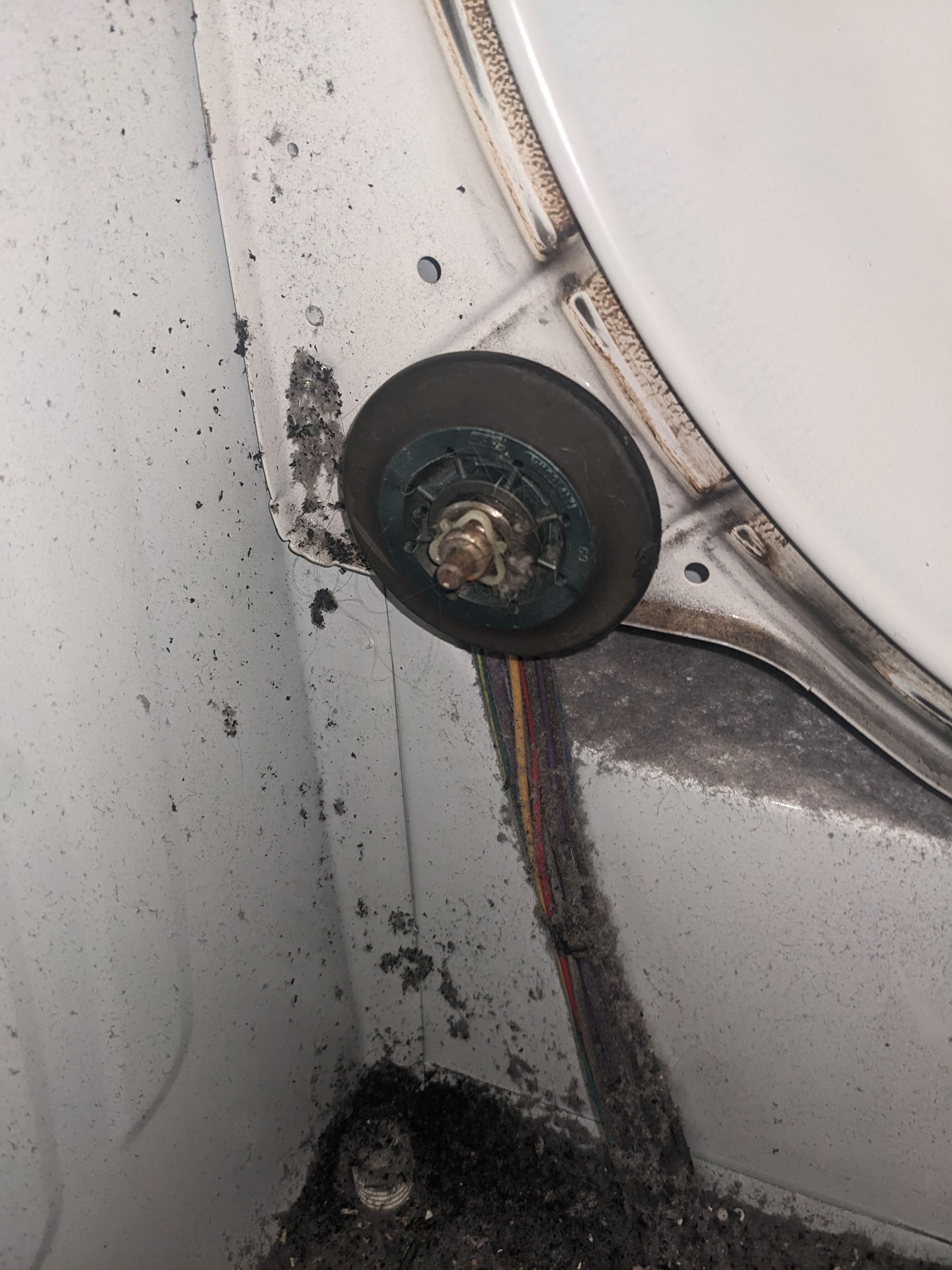 Close-up of a corroded black wheel or fastener on a dirty metal surface with rust streaks.