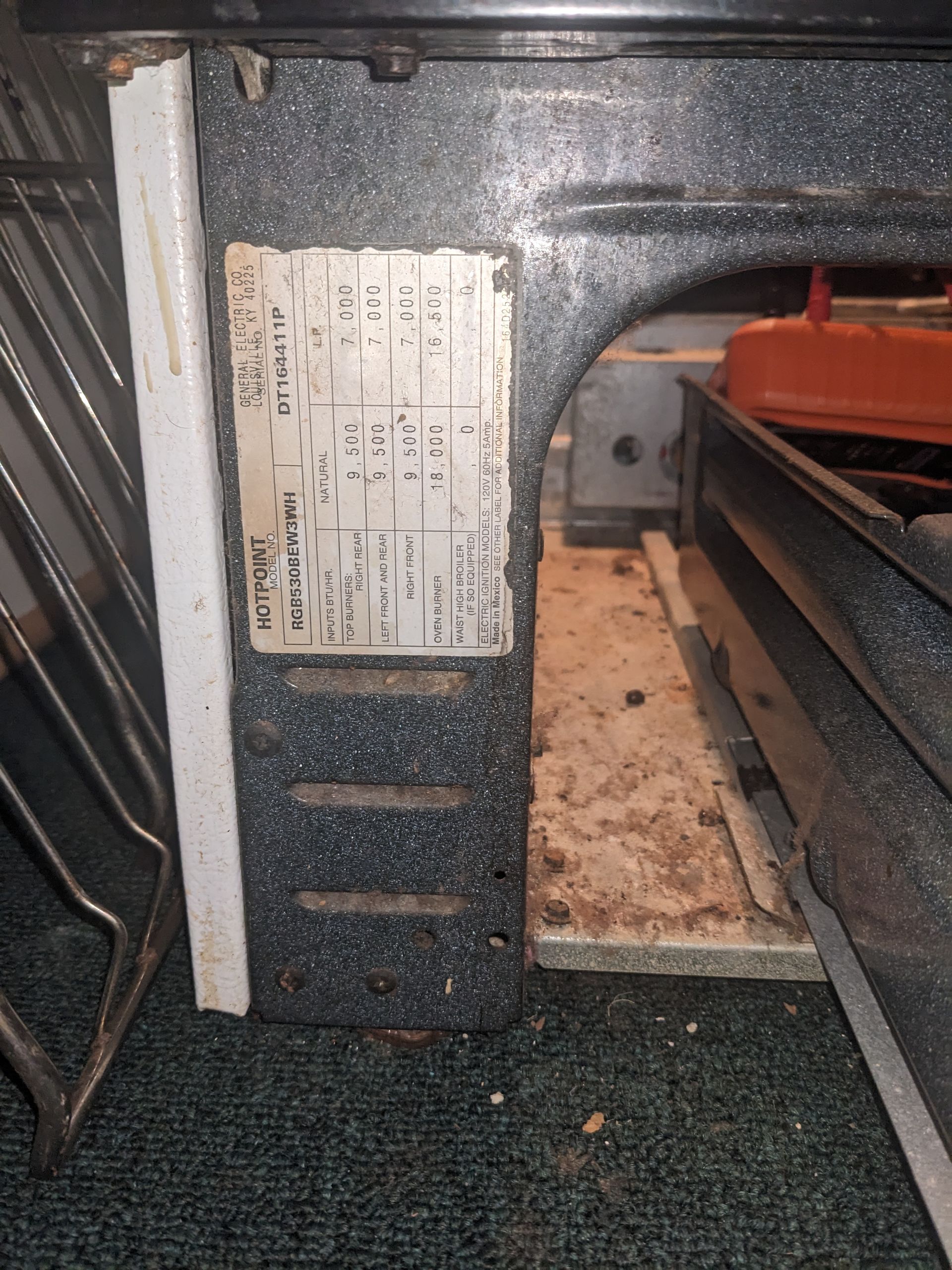 Close-up of a dusty appliance interior with a metal label and a circular opening on the right.