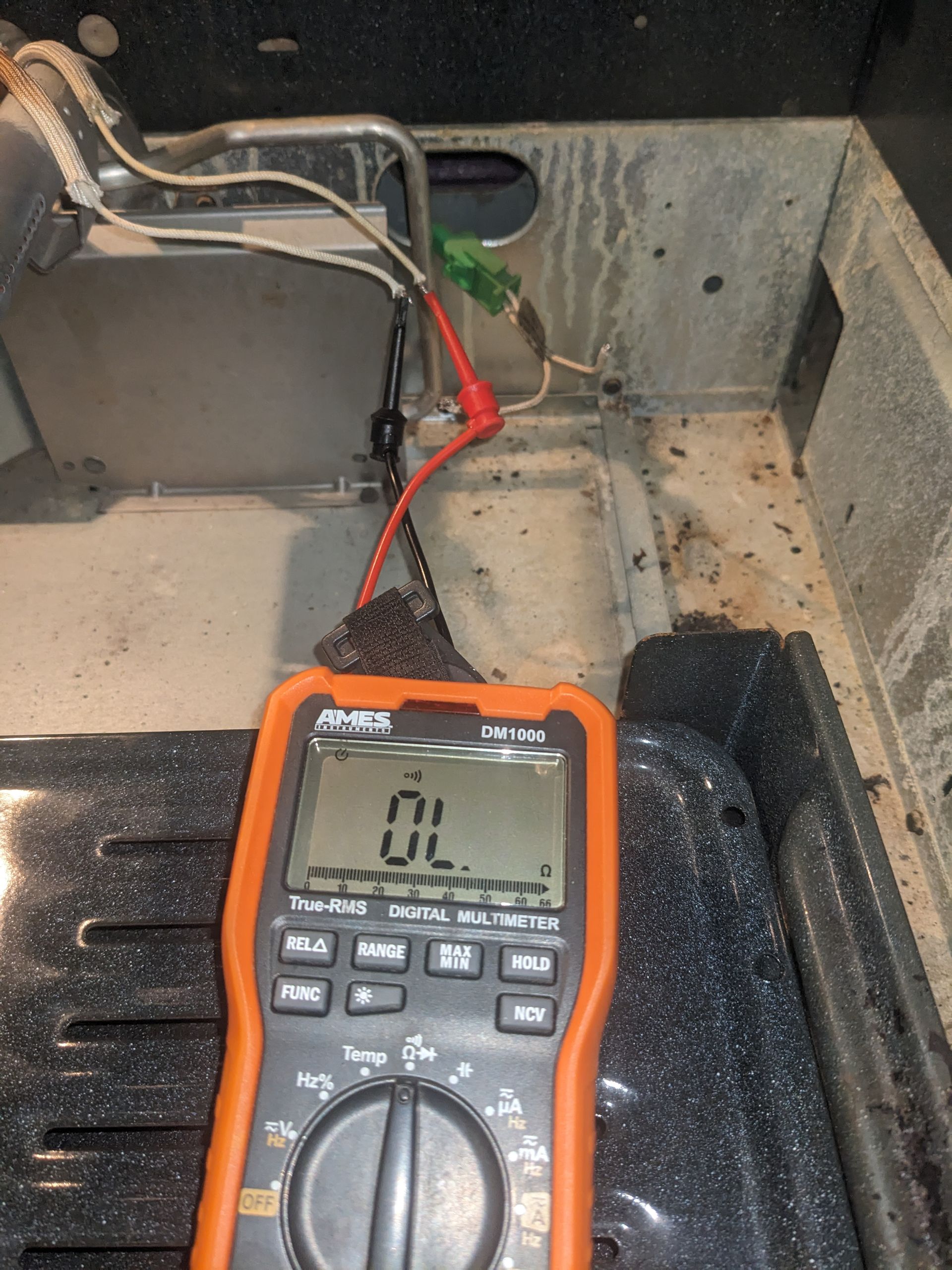 Orange digital multimeter testing wires inside an appliance, showing a low reading.