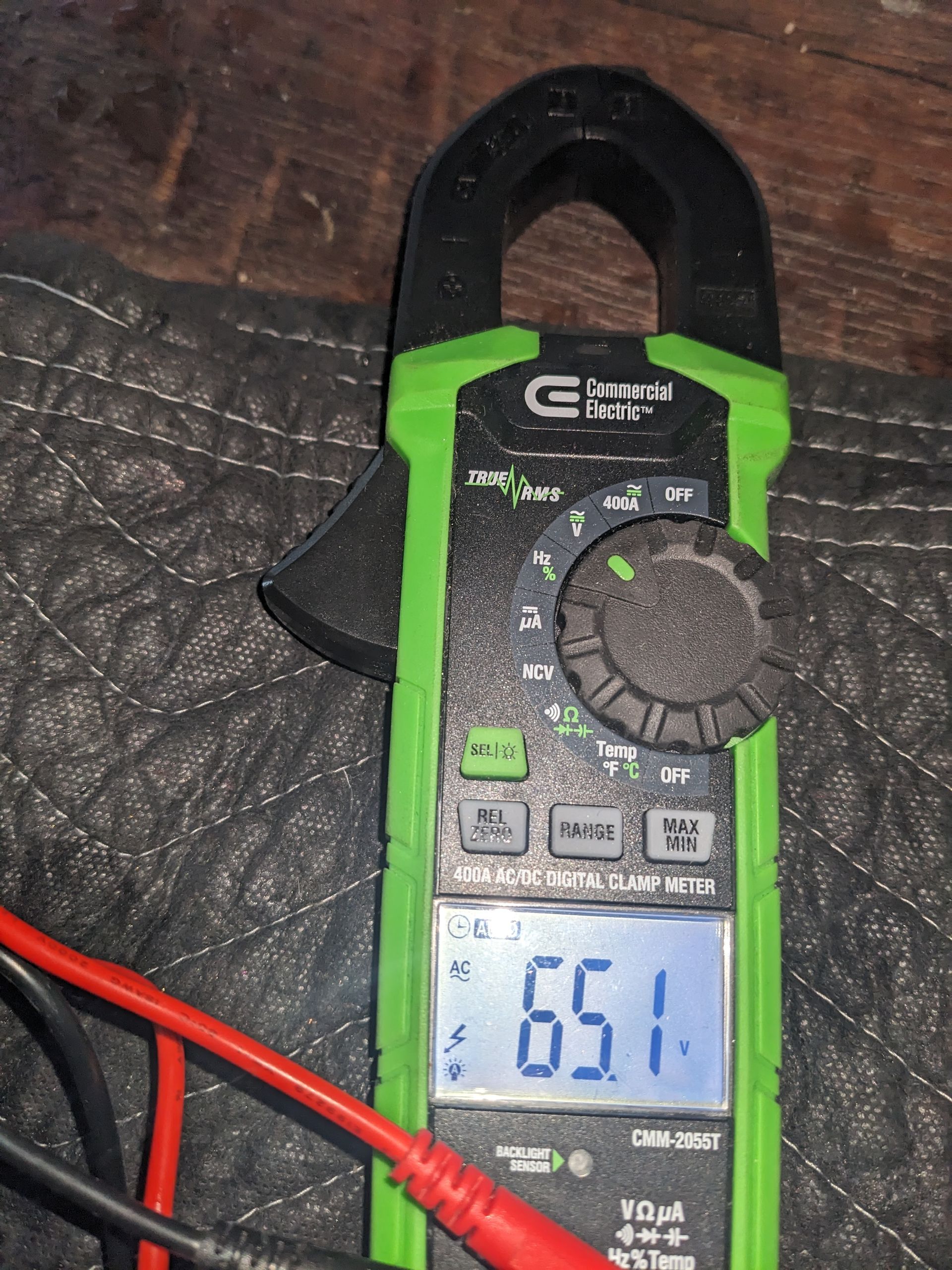 Green clamp meter on a dark surface, showing a digital reading of 65.1