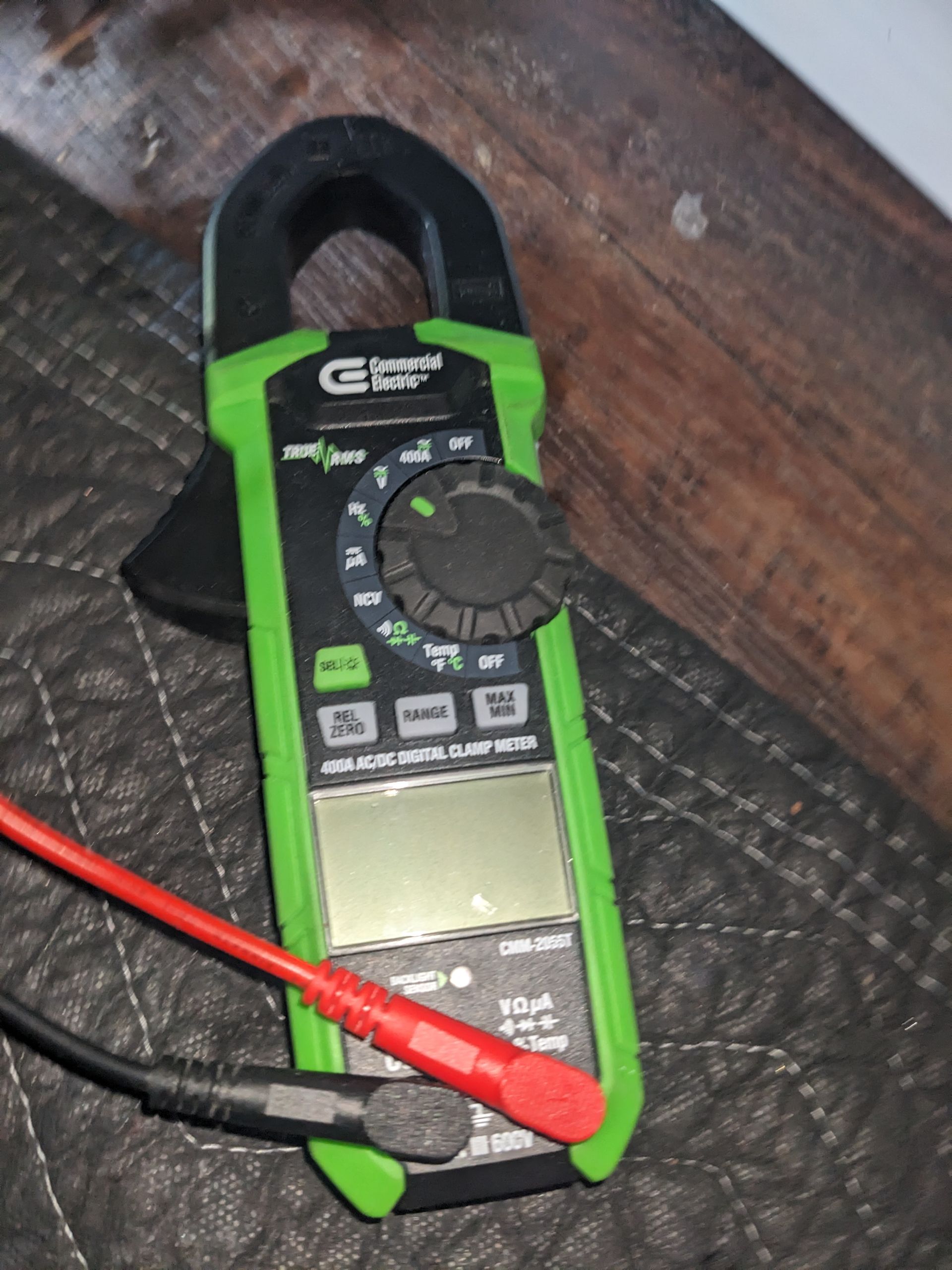 Green digital clamp multimeter with red and black probes on a wooden surface