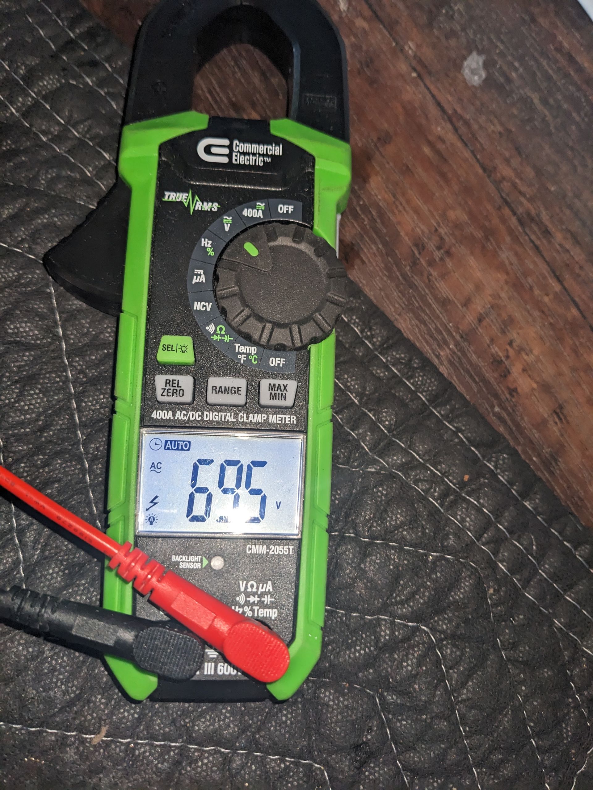 Green digital multimeter on a dark surface, showing 69.9 on the display with red and black probes attached