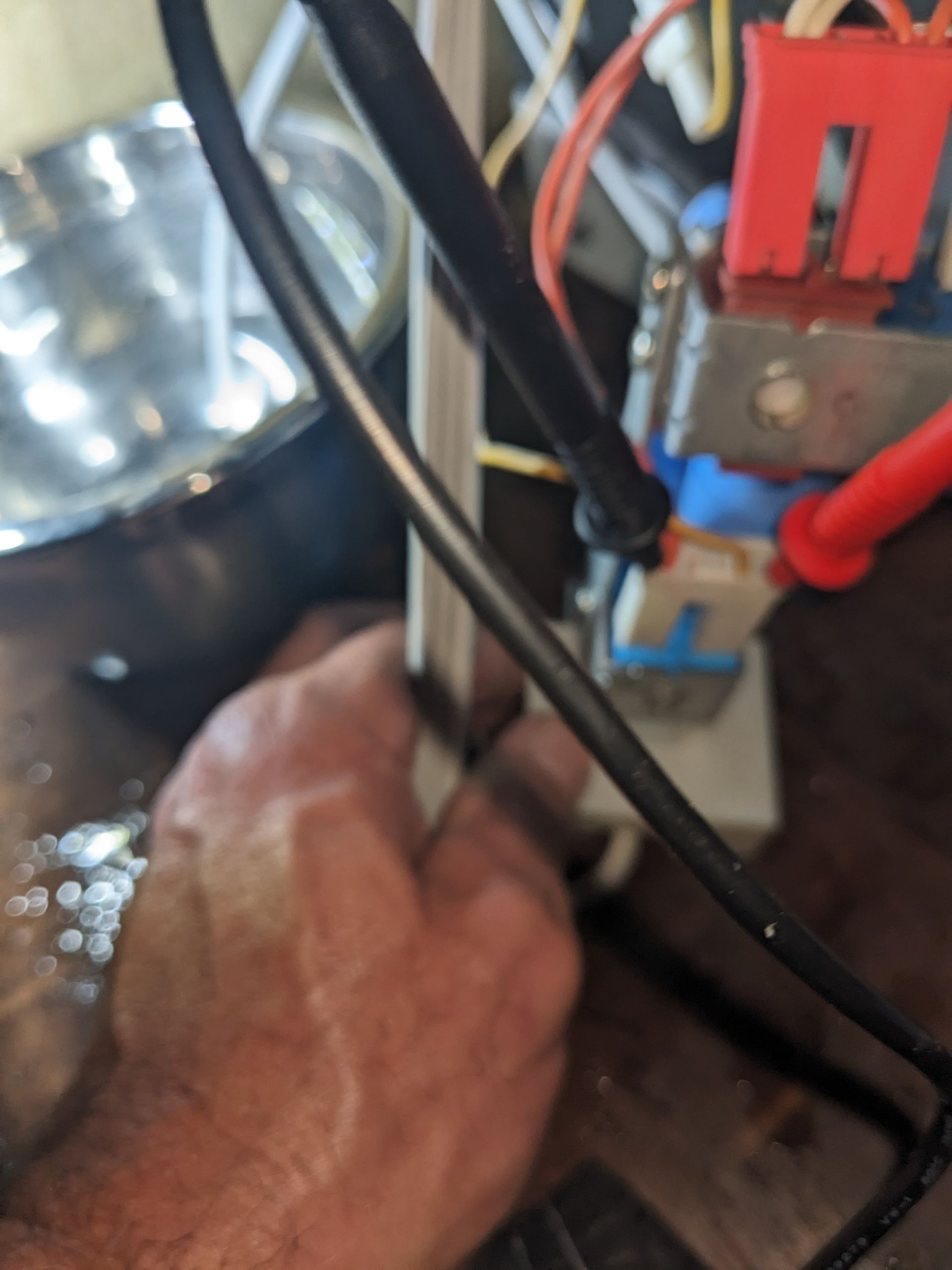 Hand working inside an electrical panel with red and black wires and a metal switch assembly