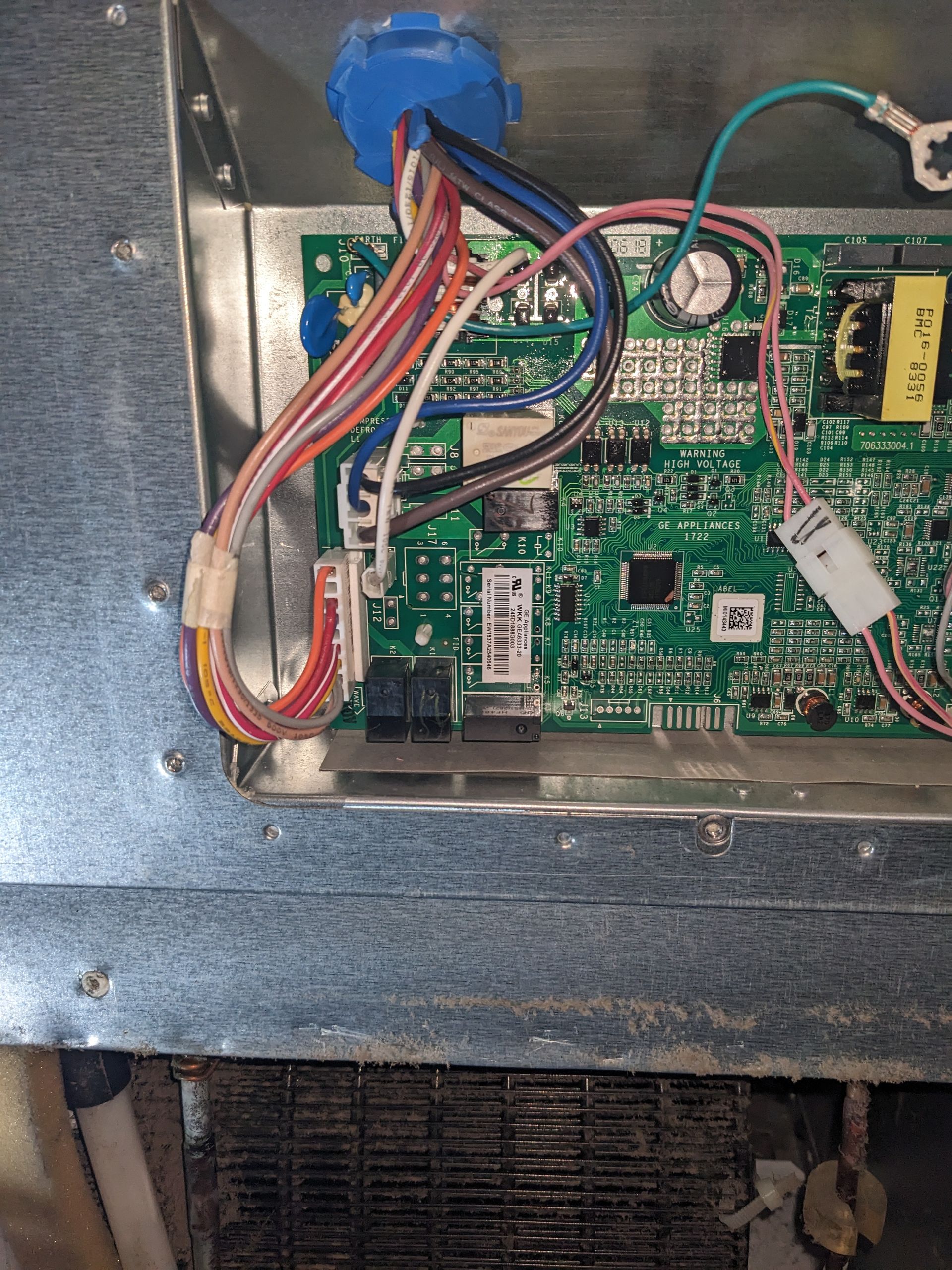 Open metal panel with tangled red and white wires connected to a green circuit board inside a machine