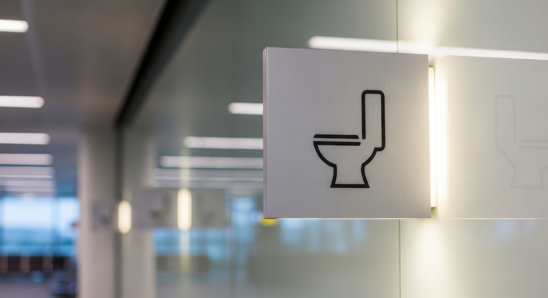Restroom sign with a toilet icon on a frosted glass wall in an office hallway