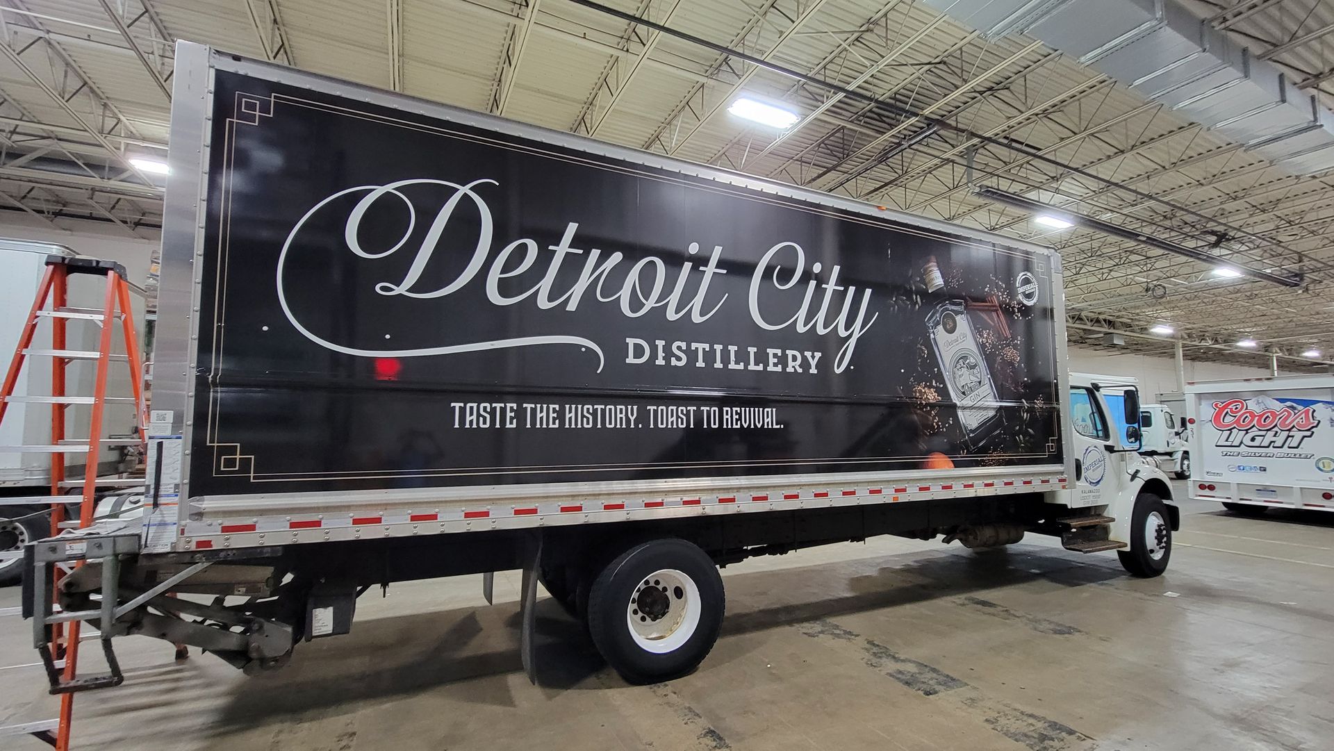 Detroit City Distillery truck with black wrap, inside a garage. White lettering on the side, red accents.