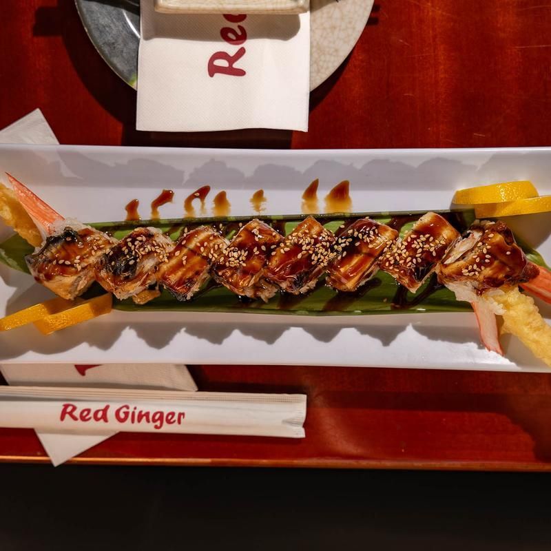 Glazed skewered seafood on a white tray with green garnish and red Ginger chopsticks