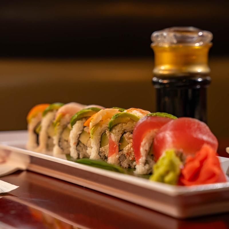 Sushi rolls on a white platter with soy sauce and pickled ginger on a wooden table