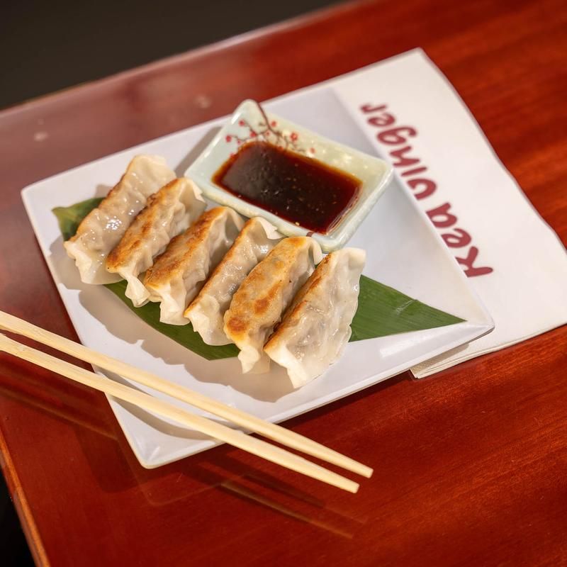Gyoza dumplings on a white plate with soy sauce, chopsticks, and a folded napkin on a wooden table