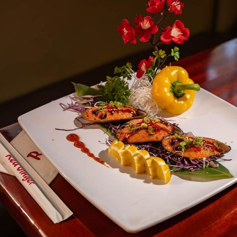 Grilled skewers on a white plate with lemon wedges, bell pepper, and red flowers on a dark table