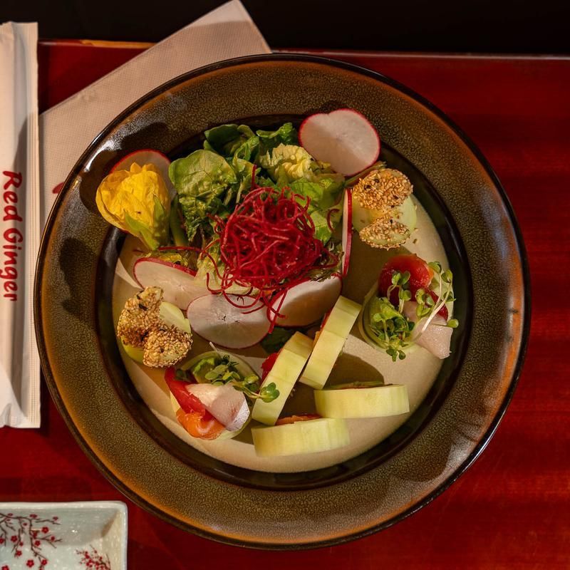 Colorful salad bowl with vegetables, greens, and shaved garnish on a red tablecloth
