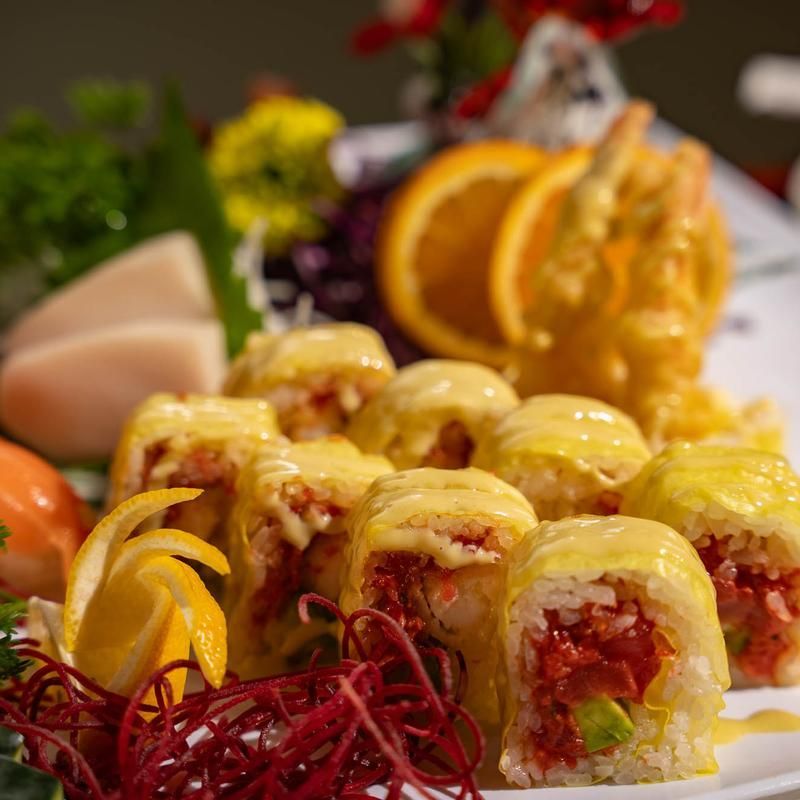 Assorted sushi rolls with yellow toppings, orange slices, and garnishes on a plated appetizer tray