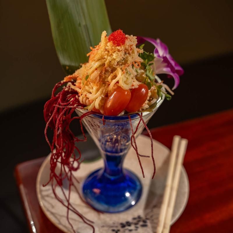 Blue glass dessert cup with shaved garnish and cherry on a plate, served with chopsticks