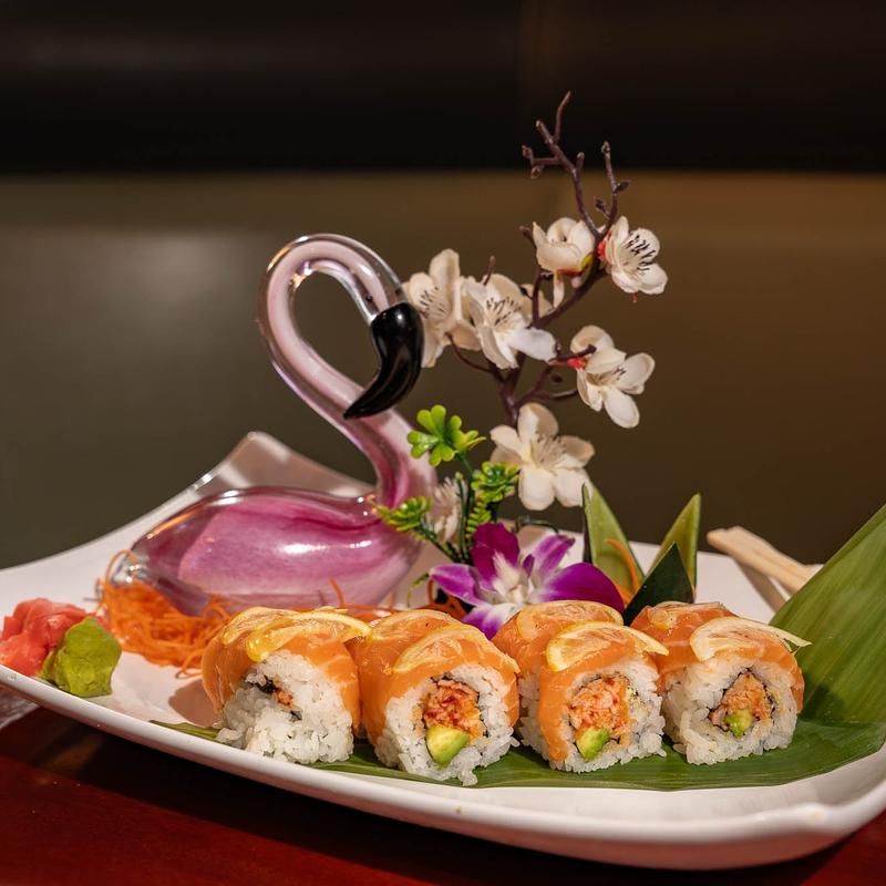 Sushi rolls with pink swan-shaped sauce dish and white blossoms on a white plate
