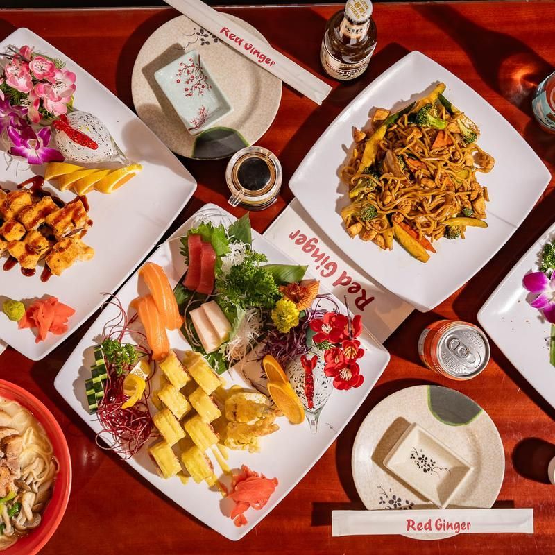 Top-down view of assorted Chinese dishes on a red restaurant table with plates, bowls, and drinks
