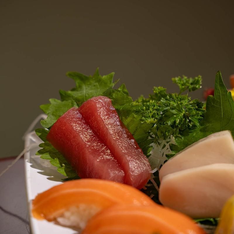 Assorted sushi sashimi on a plate with garnish, including salmon, tuna, and scallops
