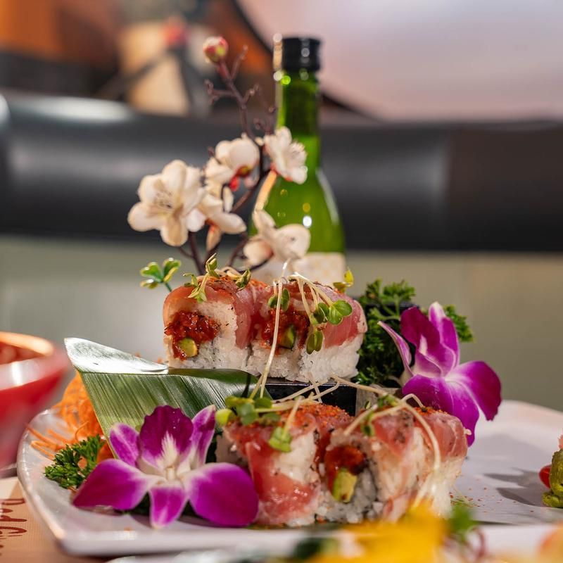 Sushi rolls garnished with purple orchids on a table, with a green bottle blurred in the background