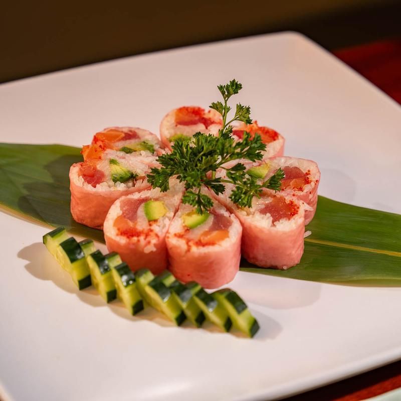 Sushi rolls arranged on a white plate with green leaf garnish and cucumber slices