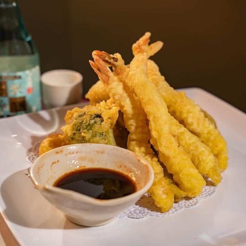 Plate of tempura shrimp and vegetables with dipping sauce on a white dish, close-up on a table