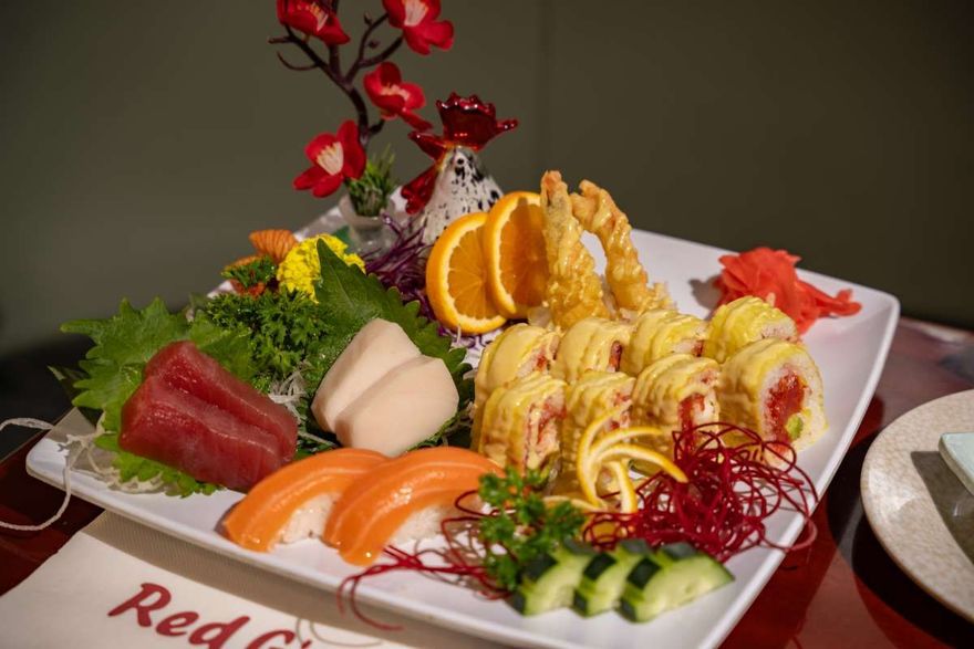 Assorted sushi and sashimi platter with orange slices and garnishes on a white plate
