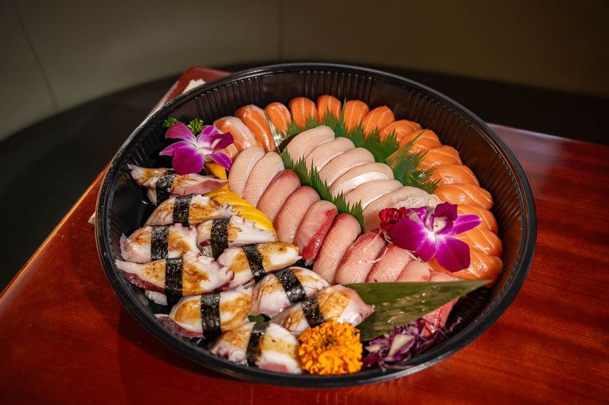 Assorted sushi platter with sashimi, rolls, and garnish on a black tray