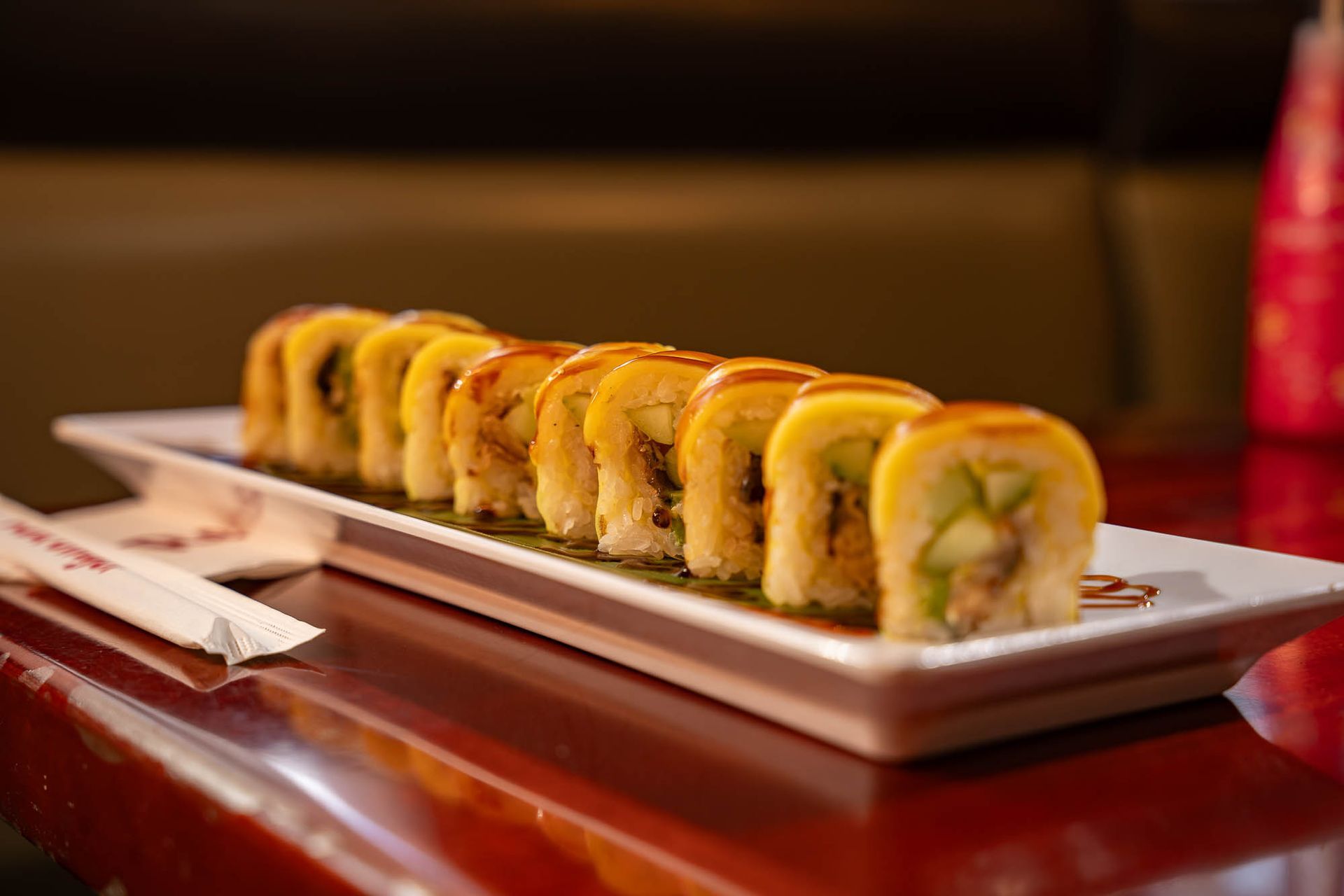 Sushi rolls on a white rectangular plate on a glossy red table, with chopsticks beside them.