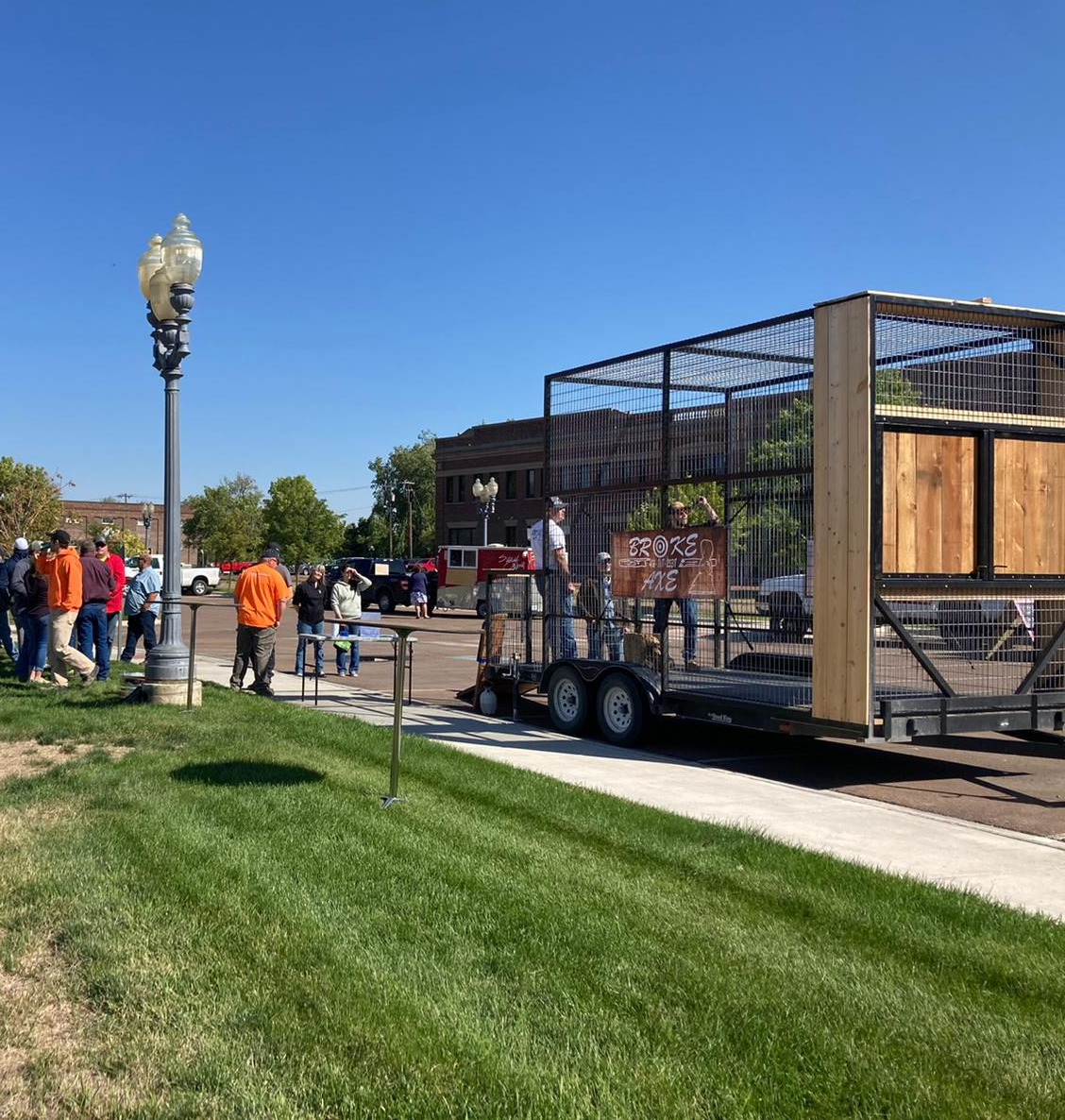 Workers beside a trailer hauling a metal cage structure on a sunny street