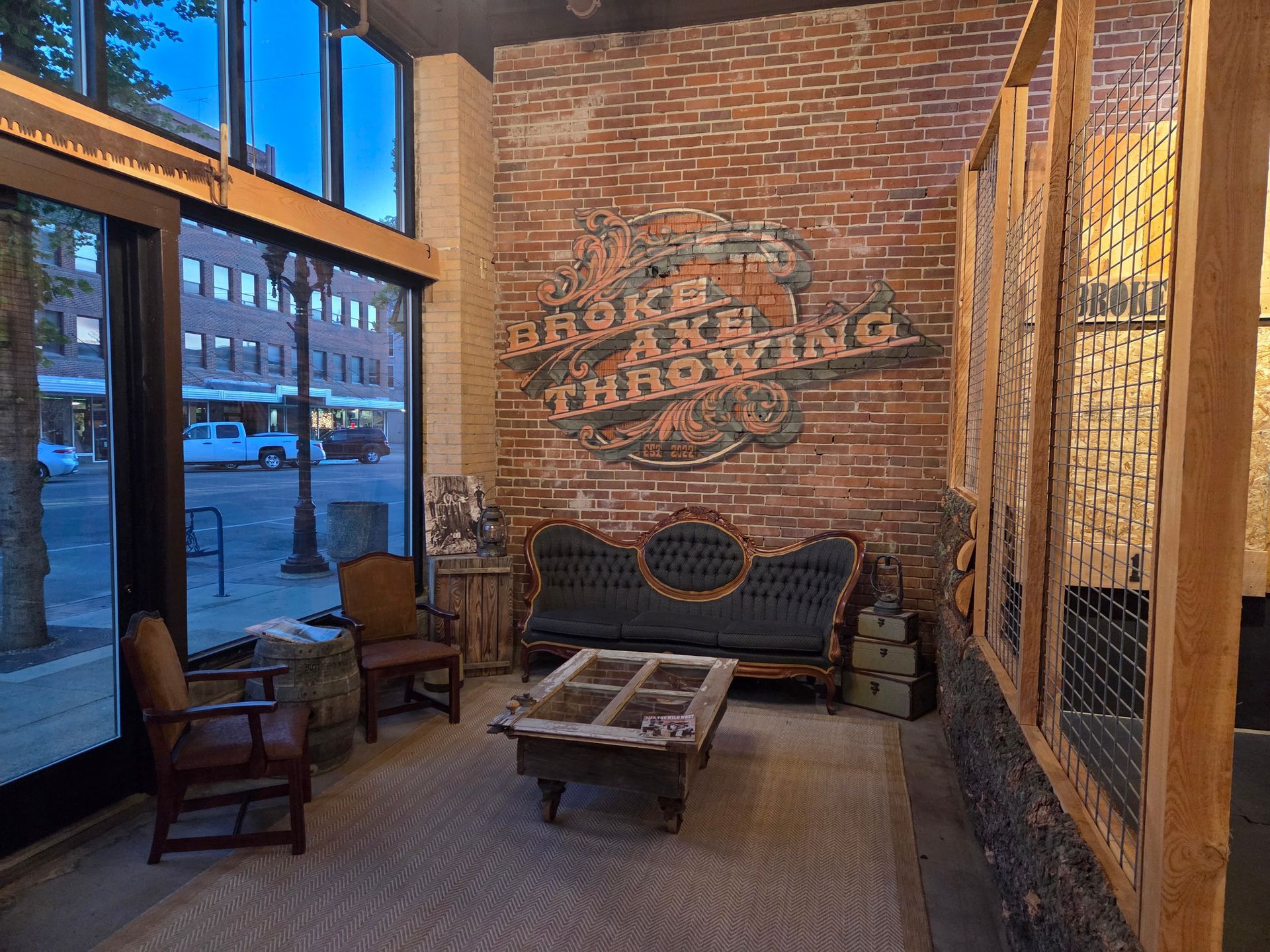 Brick-walled café corner with chairs, a small table, and a bench by large windows at dusk