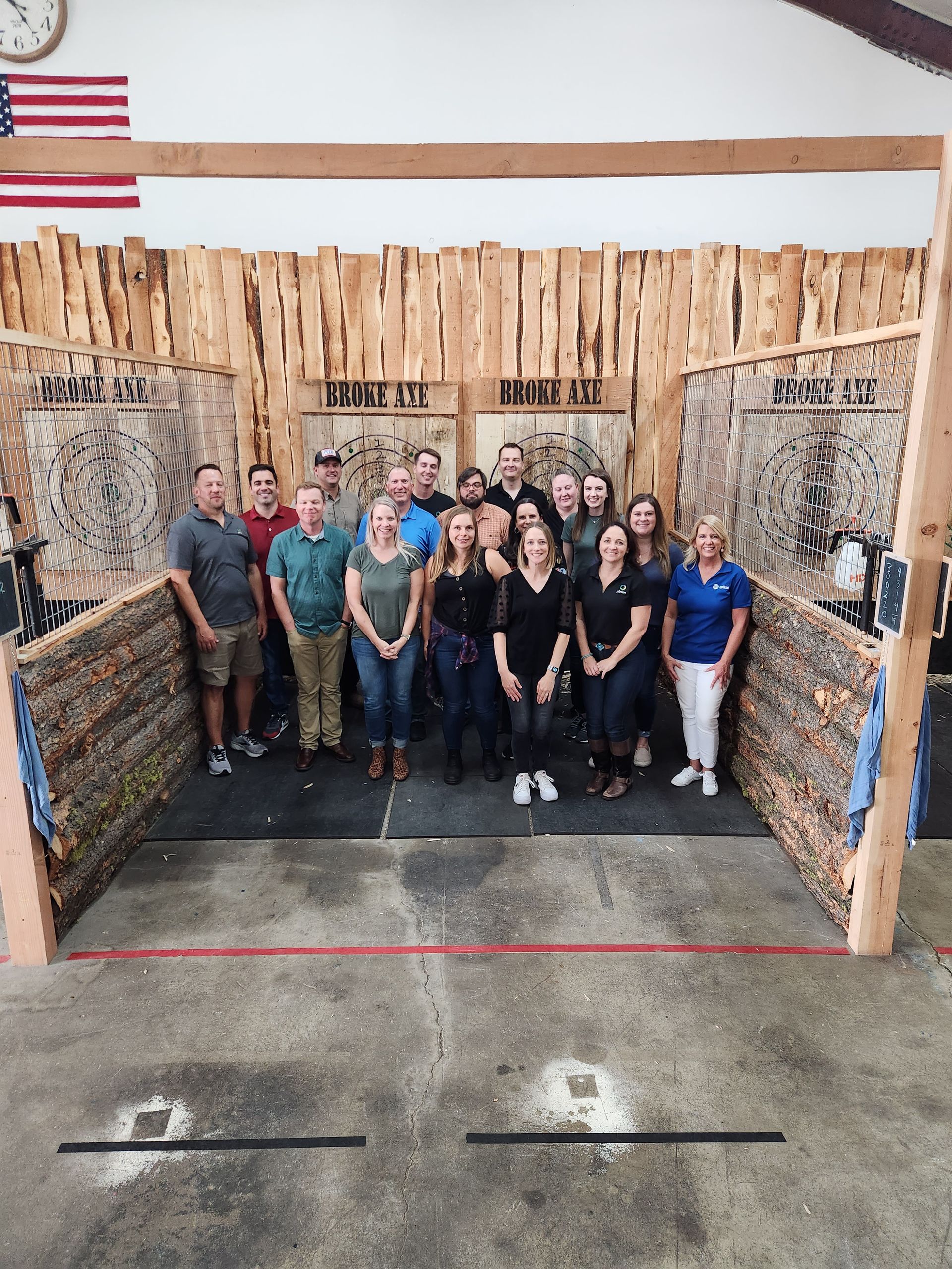 Group posing in a wooden indoor arena with a U.S. flag on the wall behind them.