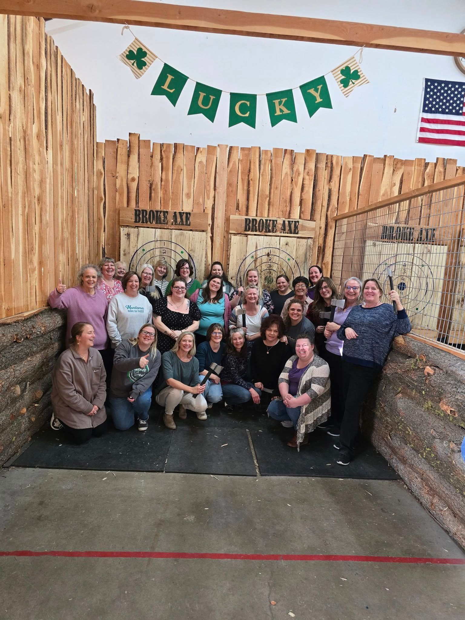 Group posing beneath a green “Lucky” banner inside a rustic bamboo-themed setting, with a U.S. flag nearby.