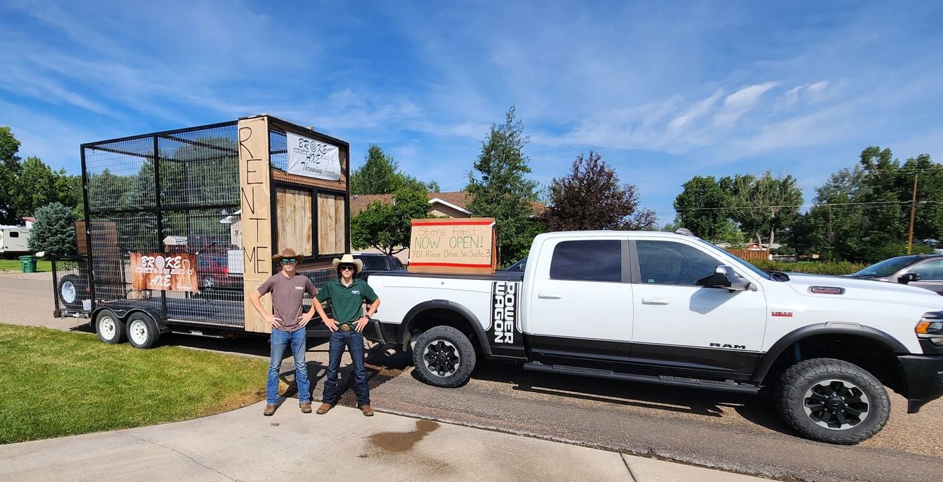 White pickup truck parked on a street beside people and a trailer in a sunny yard