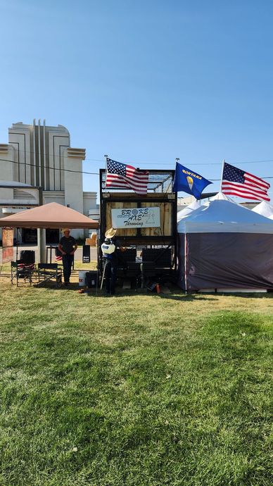 Flags waving beside a small outdoor kiosk in a grassy park under a clear blue sky