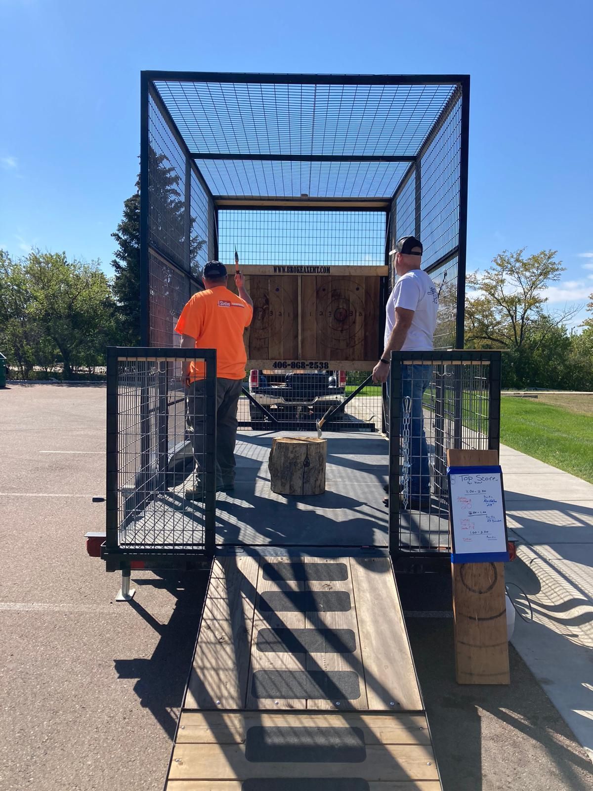 Two people on a metal ramp beside a trailer in a parking lot under a blue sky