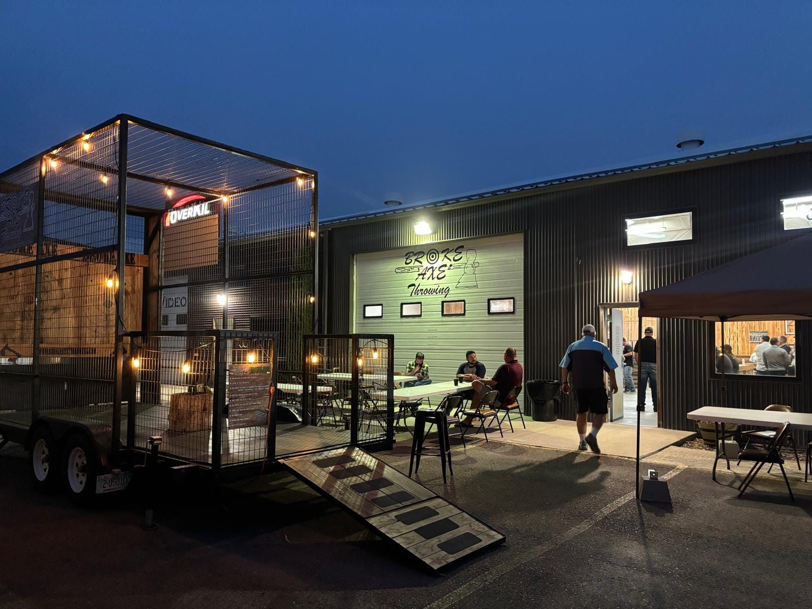 Outdoor food truck courtyard at dusk with string lights, tables, and people near a lit building