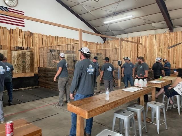 People standing in an indoor axe-throwing range with wooden walls and targets.