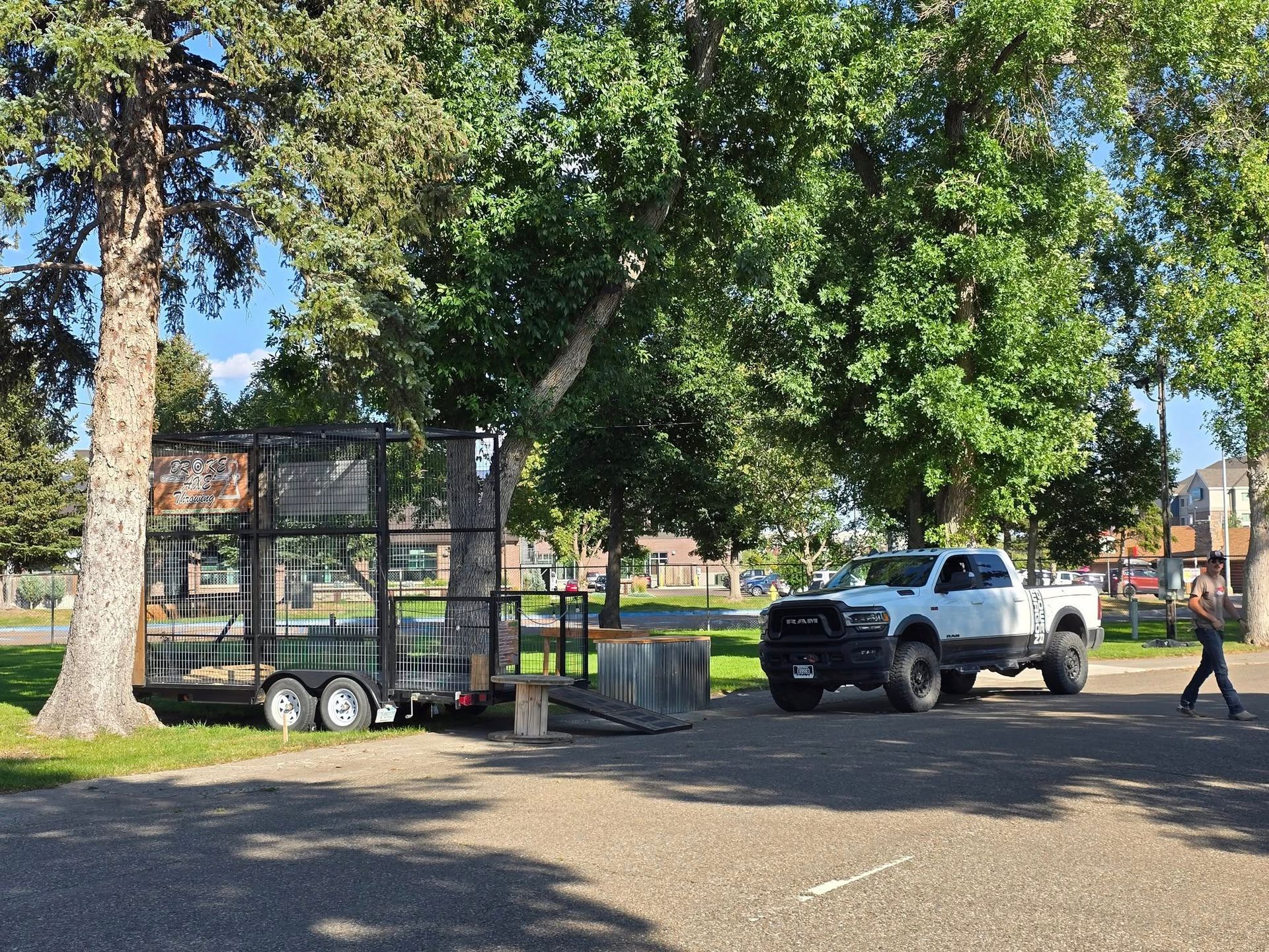 Silver pickup truck parked near a gated area in a sunny park, with a person walking nearby.