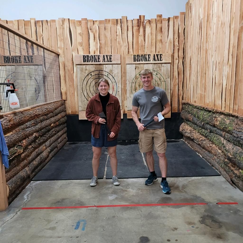 Two people standing at an axe-throwing lane with wooden targets and a log-lined backdrop