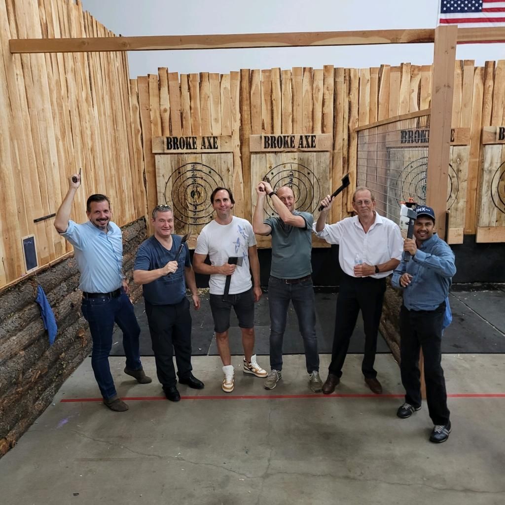 Six people pose with drinks in front of a wooden wall marked “Wheeler Ave” and “Beyond Ave.”