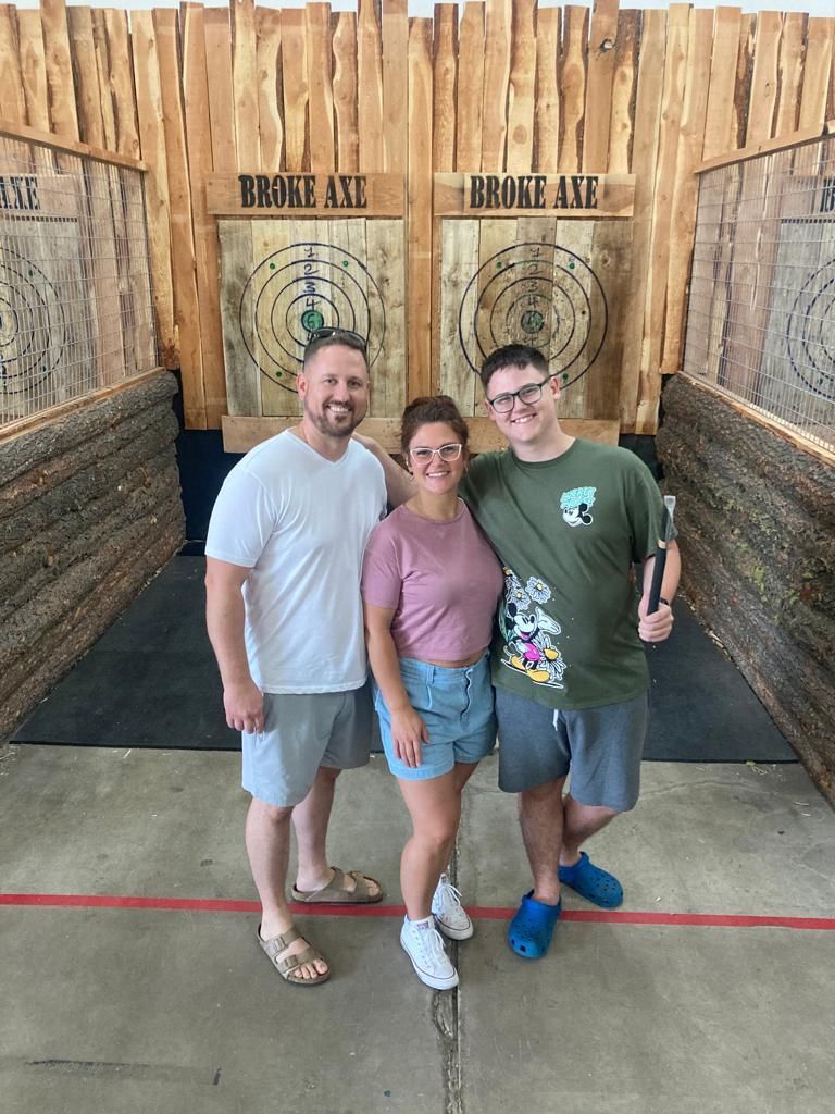 Three people posing in front of axe-throwing targets at an arcade.