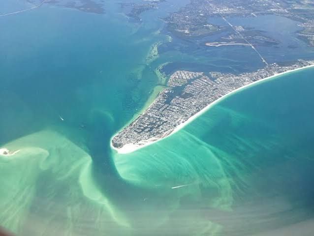 Aerial view of a narrow sandy peninsula with turquoise water and coastal buildings.