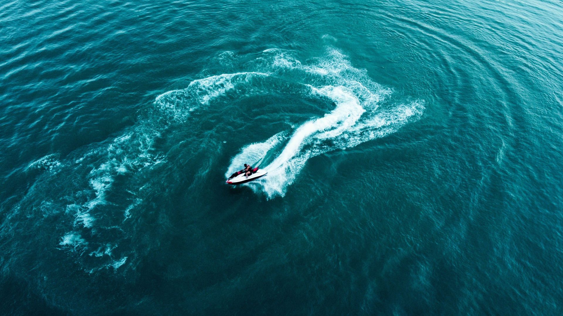 A jet ski speeds across teal ocean water, leaving a white wake behind.