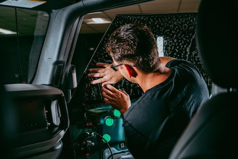 A person in a black shirt applies window tint to the interior glass of a vehicle.