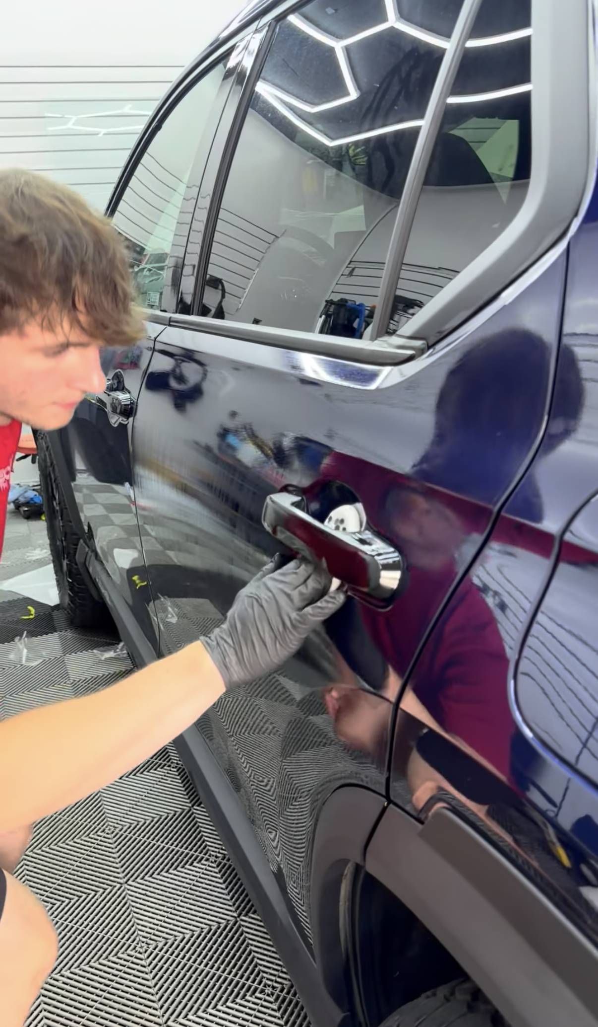 Person polishing a dark blue car door with a cloth in a garage or detailing shop