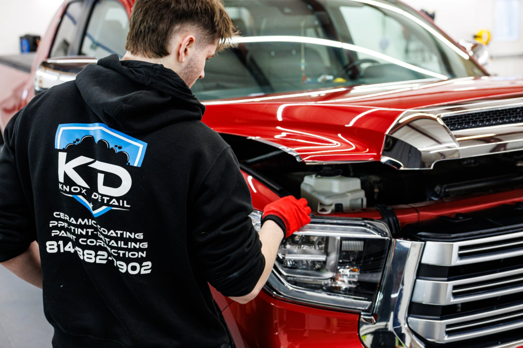 Mechanic inspecting the front of a red pickup truck in a garage