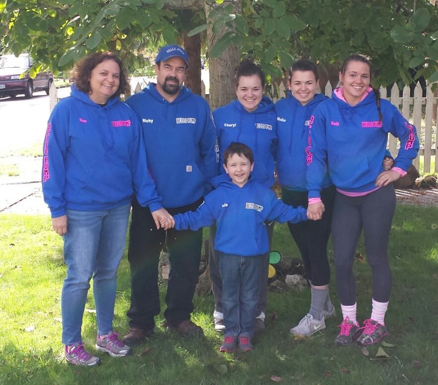 Six people in blue hoodies holding hands in front of a tree and white fence. Six people in blue hoodies holding hands in front of a tree and white fence.