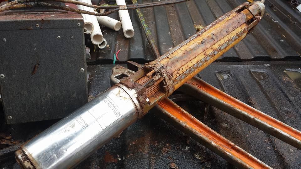 Rusty submersible water pump on a dirty metal surface, possibly a truck bed. Rusty submersible water pump on a dirty metal surface, possibly a truck bed.