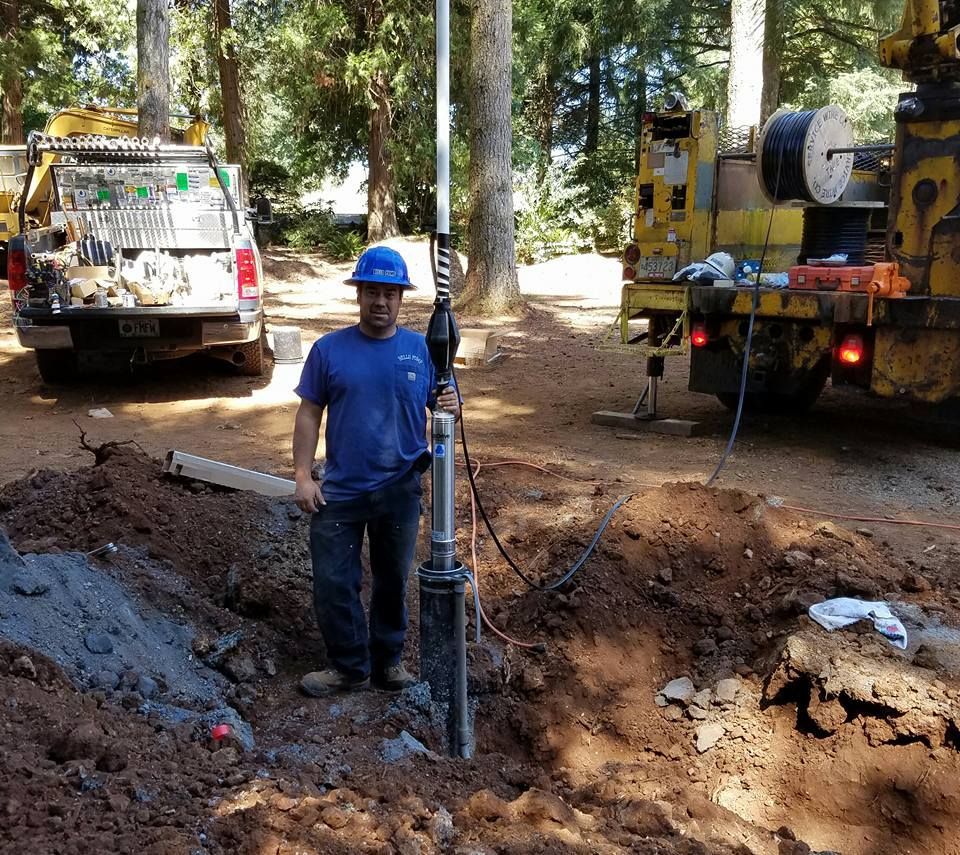 Man in blue shirt and hard hat holding well equipment near trucks and excavation. Man in blue shirt and hard hat holding well equipment near trucks and excavation.